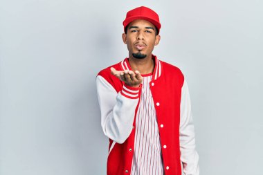 Beyzbol üniforması giymiş genç Afro-Amerikan bir adam kameraya bakıp havada bir öpücük savuruyor ve sevimli ve seksi oluyor. aşk ifadesi. 