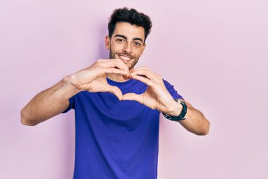 Gündelik tişört giyen, aşık gülümseyen, elleriyle kalp sembolü yapan genç bir İspanyol. romantik kavram. 
