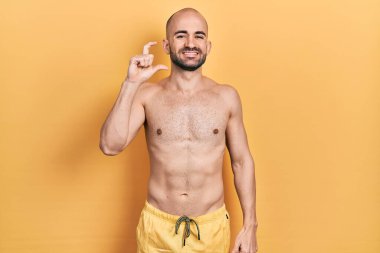 Mayo giyen genç kel adam gülümsüyor ve kendine güveni tam el hareketi yapıyor parmaklarıyla işaret yapıyor ve kameraya bakıyor. ölçüm kavramı. 