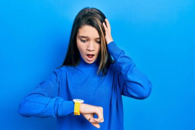 Balıkçı yaka kazak giyen genç esmer kız saate bakıyor endişeli, geç kalmaktan korkuyor. 