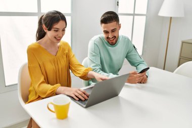 Laptop ve akıllı telefon kullanan genç İspanyol çift evde kahve içiyor..