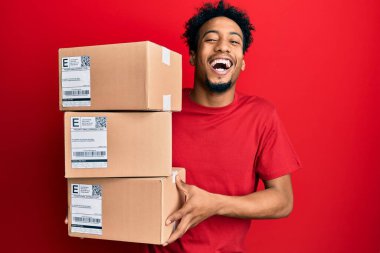 Sakallı, teslimat paketleri taşıyan ve kahkahalarla gülen genç Afrikalı Amerikalı bir adam.. 