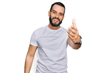 Sakallı, günlük beyaz tişörtlü genç adam dostça bir selamlama ve hoş geldin hediyesi olarak el sıkışma sunuyor. başarılı iş. 