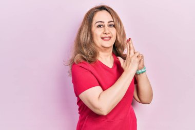 Orta yaşlı beyaz kadın, gündelik giysiler giyip, el hareketleriyle sembolik silah tutuyor, cinayet silahlarıyla oynuyor, kızgın suratlı. 