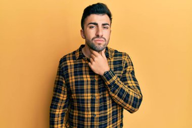 Günlük giysiler giyen genç İspanyol adam ağrılı boyuna dokunuyor, grip, mantar ve enfeksiyon yüzünden boğaz ağrısı çekiyor. 