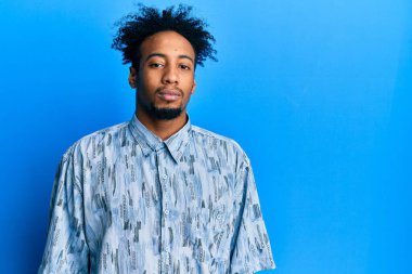 Sakallı, günlük kıyafetler giyen, yüzünde ciddi bir ifadeyle rahatlamış genç bir Afrikalı Amerikalı. Basit ve doğal bir şekilde kameraya bakıyorsun.. 