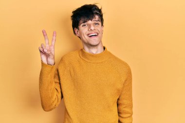 Yakışıklı hippi genç adam gündelik sarı süveter giyiyor ve iki numarayı gösterip gülümserken kendinden emin ve mutlu.. 