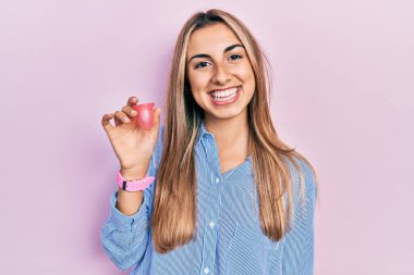 Güzel İspanyol kadın elinde regl fincanı tutarken pozitif ve mutlu görünüyor ve kendine güvenen bir gülümsemeyle dişlerini gösteriyor. 