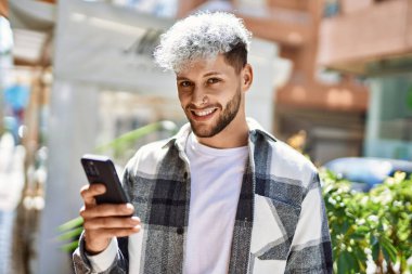 Genç İspanyol adam şehirde akıllı telefon kullanarak mutlu gülümsüyor..