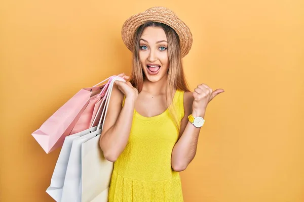 Jovem Loira Segurando Sacos Compras Apontando Polegar Para Lado Sorrindo — Fotografia de Stock