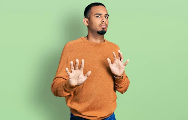 カジュアルな服を着た若いアフリカ系アメリカ人男性は 恐怖と嫌な表情で拒否と否定を示す手のひらを離れて移動します 止めて禁止する — ストック写真