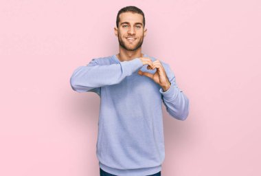 Gündelik kıyafetler giyen, aşık gülümseyen, elleri ile kalp sembolü yapan genç beyaz bir adam. romantik kavram. 