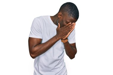 Genç Afro-Amerikalı bir adam günlük beyaz tişört giyiyor ve ağlarken suratını ellerle kapatıyor. depresyon kavramı. 