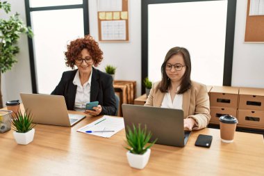 Ofiste çalışan iki kadın grubu. Olgun kadın ve Down sendromlu kız kapsayıcı takım çalışması yapıyor..