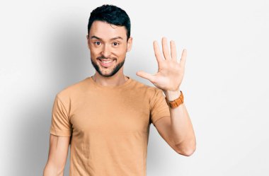Sakallı, sıradan tişörtlü İspanyol bir adam beş numarayı gösterip işaret ederken kendinden emin ve mutlu bir şekilde gülümsüyor.. 
