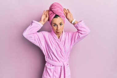 Duş başlığı takan ve bornoz giyen genç sarışın kadın tavşan kulağı yapıyor. Avuçlarıyla alaycı ve şüpheci görünüyor. Paskalya tavşanı konsepti. 