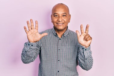 Orta yaşlı, gündelik kıyafetler giyen Latin bir adam 8 numaralı parmaklarını gösterip işaret ederken kendinden emin ve mutlu bir şekilde gülümsüyor.. 