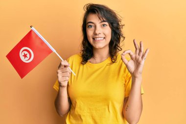 Tunus bayrağı tutan genç İspanyol kadın parmaklarıyla imza atıyor, gülümseyerek mükemmel bir sembol oluşturuyor. 