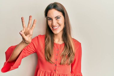 Genç ve güzel bir kadın gündelik kıyafetler giyer ve üç numaralı parmaklarıyla işaret ederken kendinden emin ve mutlu bir şekilde gülümserdi.. 