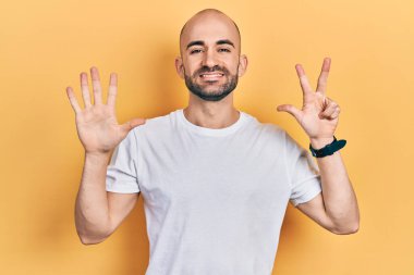 Genç kel adam, günlük beyaz tişört giyer ve 8 numaralı parmaklarıyla gülümseyerek mutlu ve kendinden emin bir şekilde onu gösterir.. 