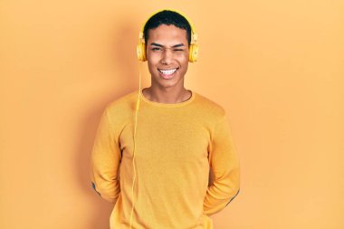 Genç Afrikalı Amerikalı adam müzik dinliyor kulaklık takıyor kameraya seksi bir ifadeyle bakıyor, neşeli ve mutlu bir yüzle.. 