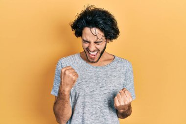 Yakışıklı, gri tişörtlü adam kolları havada ve gözleri kapalı bir şekilde başarıyı kutluyor. 