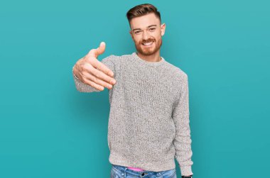 Kış süveteri giyen genç kızıl saçlı adam selamlama ve hoş geldin demek için dostça tokalaşıyor. başarılı iş. 