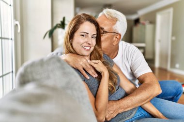 Orta yaşlı İspanyol çift mutlu bir şekilde gülümsüyor ve evdeki kanepede oturup sarılıyorlar..