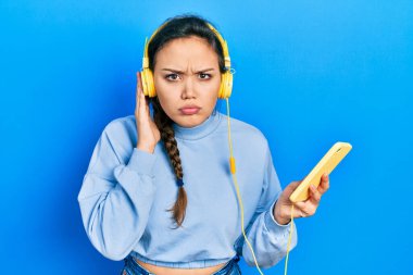 Akıllı telefon ve kulaklık kullanan genç İspanyol kız şüpheci ve gergin, sorun yüzünden surat asıyor. negatif kişi. 