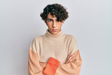 Latin kökenli genç adam sıradan bir kazak giyiyor şüpheci ve gergin, yüzünde çapraz kollu tasvip etmeyen bir ifade. negatif kişi. 