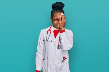 Genç Afro-Amerikan kadın doktor üniforması giyiyor ve steteskop bir gözünü eliyle kapatıyor, yüzünde kendine güvenen bir gülümseme ve şaşırtıcı bir duygu var.. 