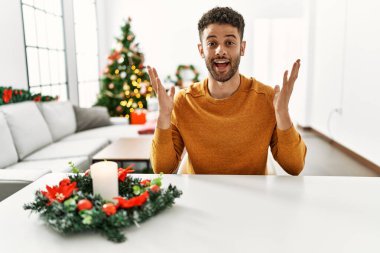 Arap genç adam Noel ağacının yanında oturmuş çılgınlığı kutluyor ve kollarını kaldırıp heyecanla haykırarak başarıya hayret ediyor. Kazanan konsept 