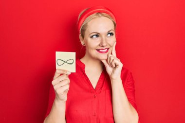 Sonsuz sembol taşıyan genç sarışın kadın. Ciddi bir yüz ifadesi. Elleri çenesinde soru soran, kafa karıştırıcı fikirleri düşünen. 