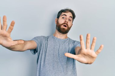 Sakallı, günlük gri tişörtlü, korku ifadesinden korkan, dehşete düşmüş beyaz bir adam. Ellerinle hareket etmeyi kes, şok içinde bağır. panik konsepti. 