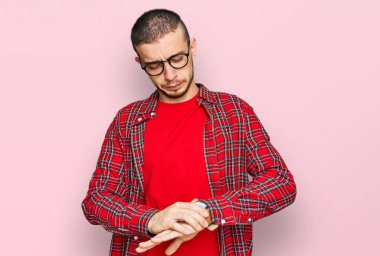 Gündelik kıyafetler giyen İspanyol genç adam kol saatini kontrol ediyor, rahat ve kendinden emin. 