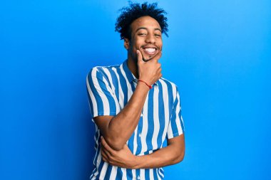 Sakallı, sıradan çizgili gömlek giyen, kameraya kollarını kavuşturup gülümseyen ve çenesini kaldıran Afro-Amerikan genç bir adam. Olumlu düşünmek. 