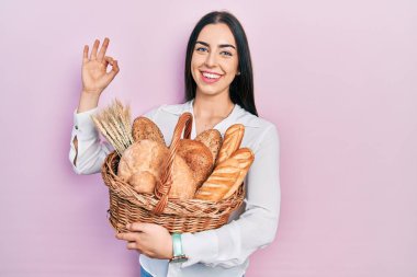 Mavi gözlü güzel kadın elinde hasırdan sepet, elinde ekmek tamam işareti yapıyor parmaklarıyla gülümseyerek mükemmel bir sembol oluşturuyor. 