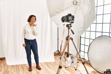 Orta yaşlı İspanyol bir kadın fotoğraf stüdyosunda modellik yapıyor. Gülümsüyor, gülümsüyor ve başparmağını kaldırıyor.. 