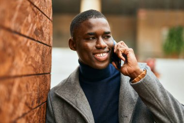 Genç Afrikalı Amerikalı gülümseyen mutlu bir adam şehirdeki akıllı telefondan konuşuyor.