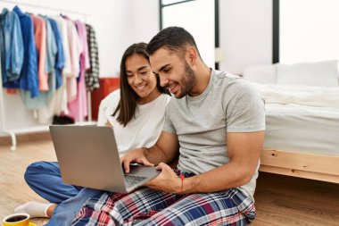 Genç Latin çift mutlu bir şekilde gülümsüyor. Yatak odasında yerde oturuyor.