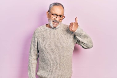 Sakallı, sıradan bir süveter giyen ve gözlüklü, mutlu bir el hareketi yapan yakışıklı bir adam. Kameraya bakıp başarıyı gösteren ifade. 