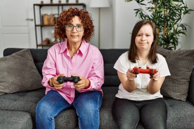 Olgun anne ve Down sendromlu kız evde video oyunu oynuyor.