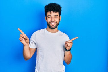 Sakallı, beyaz tişörtlü, kendine güvenen, farklı yönleri gösteren genç bir Arap. reklam için kopyalama alanı 