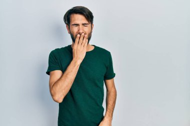 Gündelik beyaz tişört giyen genç İspanyol adam ağzını eliyle kapatmaktan sıkılmış. Huzursuz ve uykulu.. 