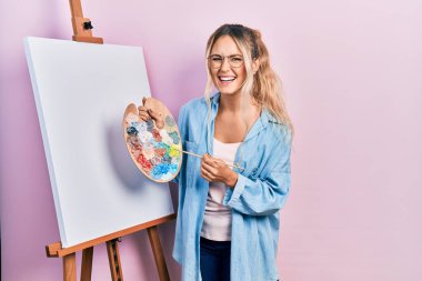 Güzel, genç, sarışın bir kadın boyacı sehpasında paletle resim çizerken ayakta duruyor ve kahkahalarla gülüyor çünkü komik, çılgınca bir şaka.. 