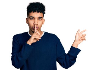 Gündelik giysiler giymiş genç Afro-Amerikalı adam sessiz olmak istiyor. Parmakları dudaklarında, elleri yandan işaret ederek. sessizlik ve gizli konsept. 