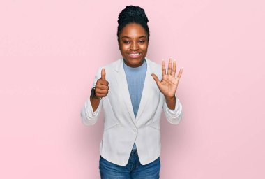 Genç Afro-Amerikan kadın iş kıyafetleri giyip altı numaralı parmaklarıyla işaret ederken kendinden emin ve mutlu bir şekilde gülümsüyor.. 