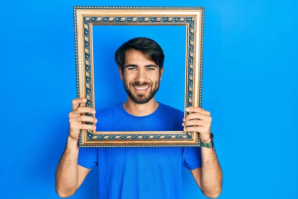 Joven Hombre Hispano Sosteniendo Marco Vacío Sonriendo Con Una Sonrisa — Foto de Stock