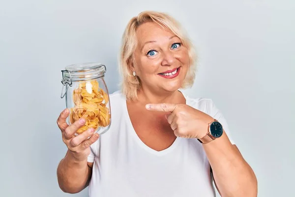 Middelbare Leeftijd Blonde Vrouw Met Ongekookte Noedels Glimlachen Gelukkig Wijzend — Stockfoto