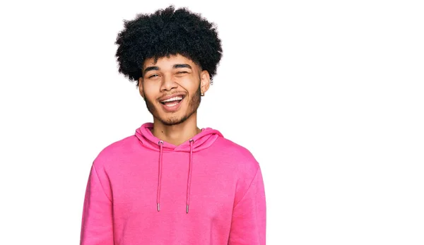 若いですアフリカ系アメリカ人男性とともにAfro髪身に着けていますカジュアルピンクのスウェットシャツウインク見ますザカメラとともにセクシー式 陽気で幸せな顔 — ストック写真